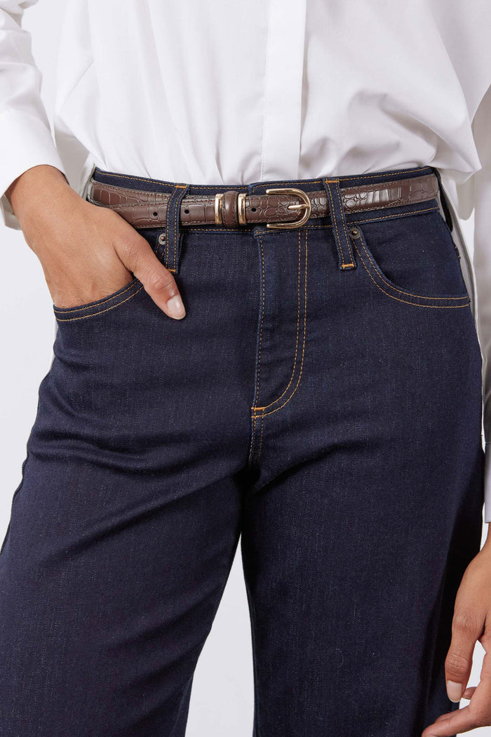 Chocolate croc-embossed belt with oval buckle on dark denim jeans at waist