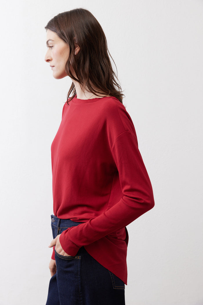 Garnet red long-sleeve top, side back view with draped hem over jeans
