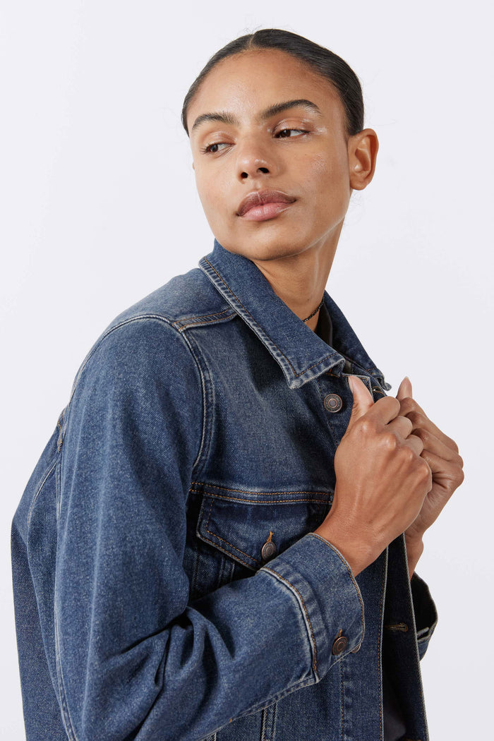 Long line denim jacket shoulder and sleeve, medium-wash blue with button cuff detail.