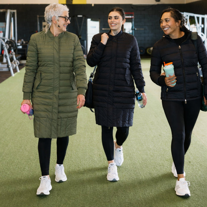 Two women wearing Moke - Lucy Cloud Touch Packable Down Jacket (LUCY) in the colour Black and another woman wearing Moke - Lucy Cloud Touch Packable Down Jacket (LUCY) in the colour Olive Green. Three friends walking together wearing their Moke Lucy jackets.