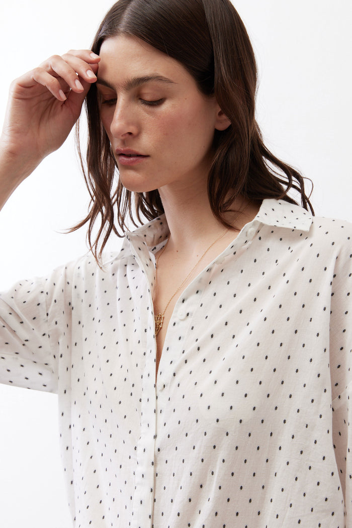 Neck and chest close-up of white oversized tunic with black dot print, button-up collar