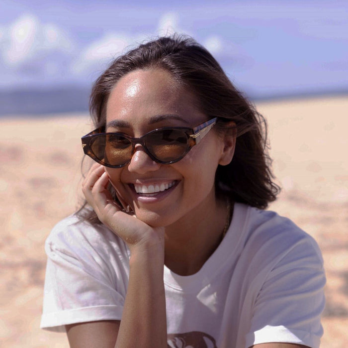 Woman wearing sunglasses and a white t-shirt with a desert landscape in the background