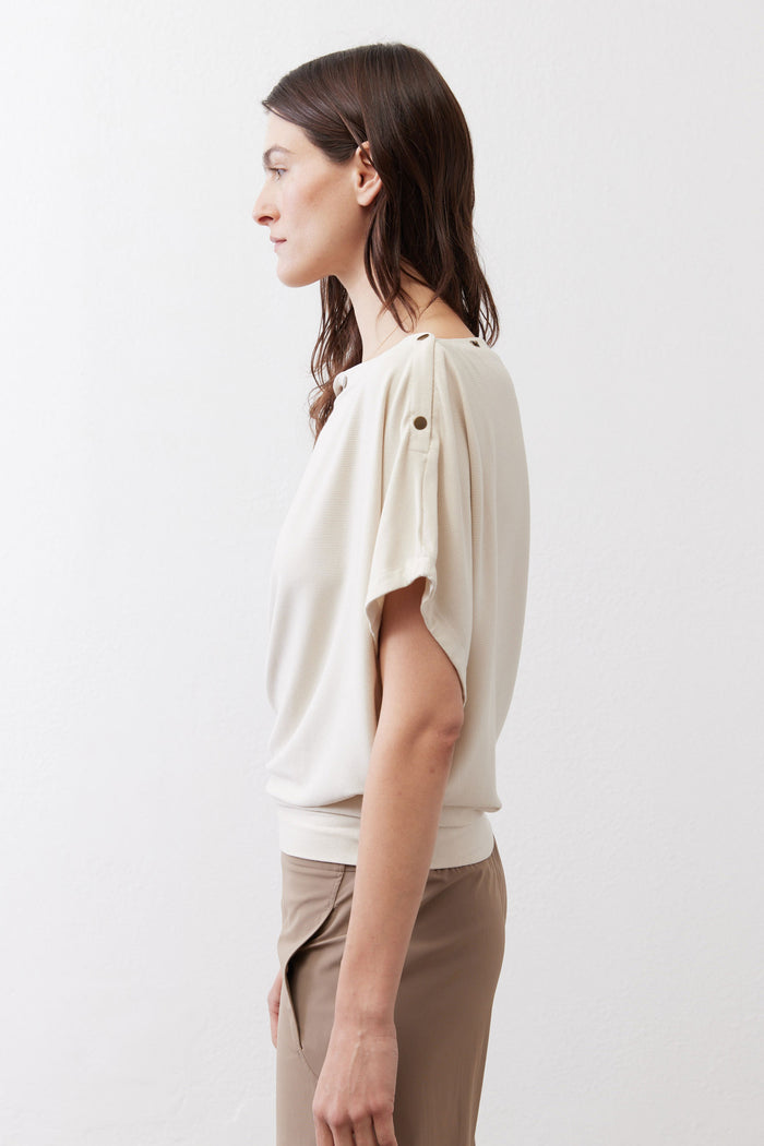 Cream short sleeve top draped with loose cap sleeves and shoulder buttons