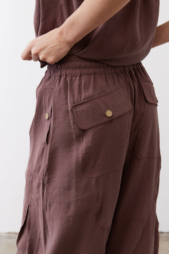 Dark brown cargo-style pocket on utility pants with snap button and stitched panel