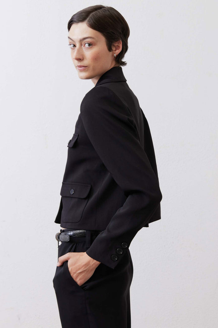 Black collared classic jacket in side view with flap pockets, button cuffs, and belt