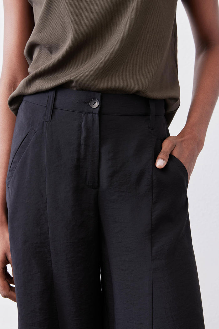Black wide-leg pants with button closure, front pockets, and relaxed pleated waist.