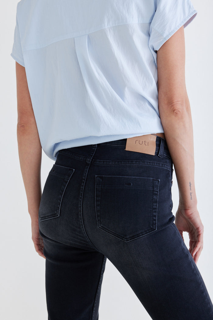 Dark fitted jeans close-up: front pocket and curved seam stitching