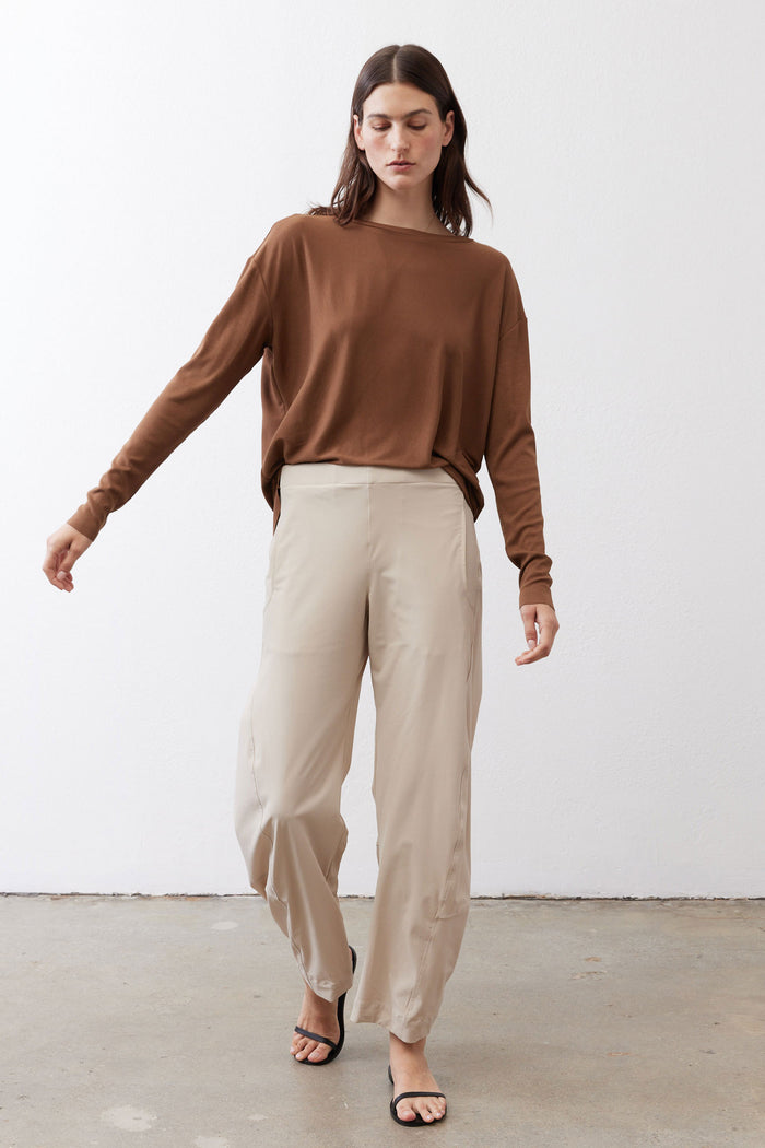 Light beige loose work pants with elastic waist and tapered ankle; model walking view.