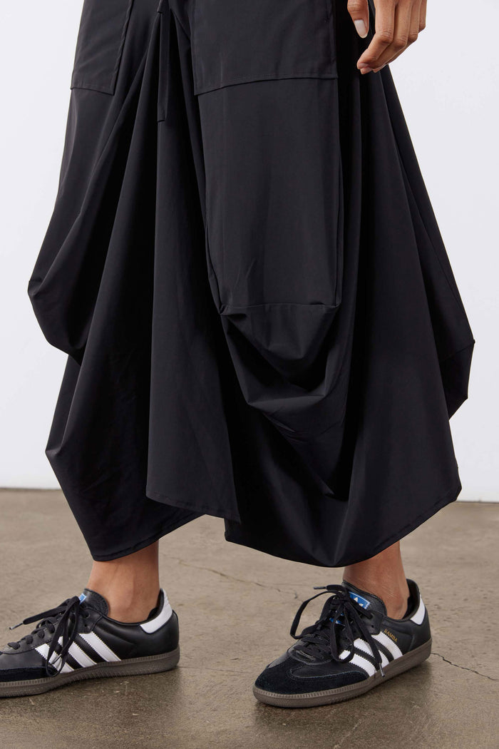 Black skirt side detail: layered drape with large pocket panel and stitched seams