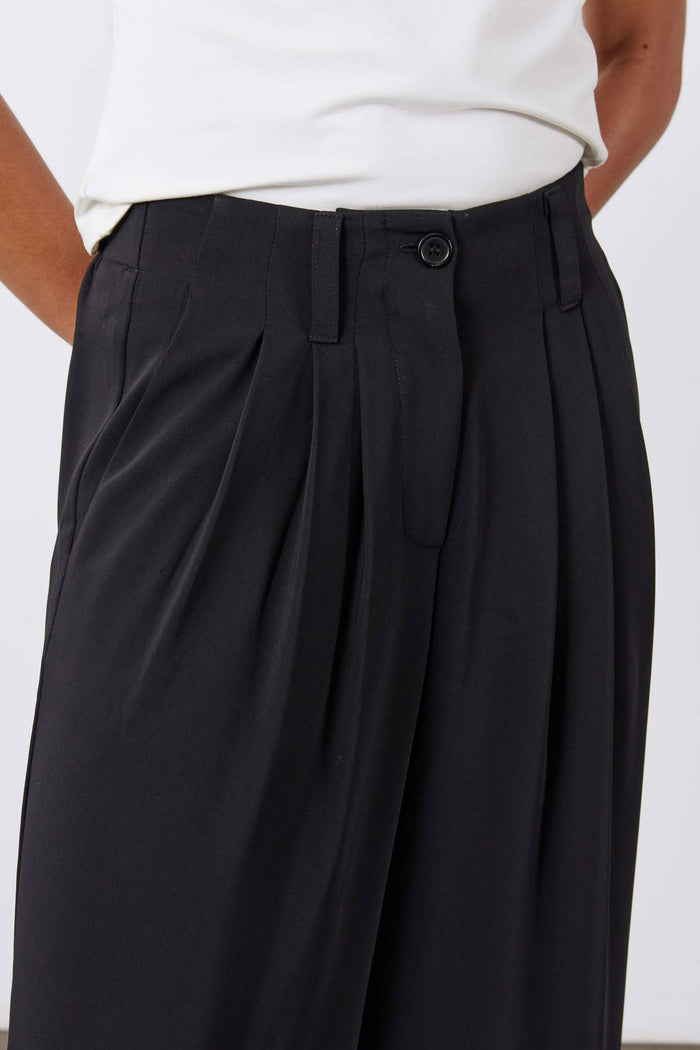 Petite black wide-leg trousers with pleats, button tab at waist, and belt loops.
