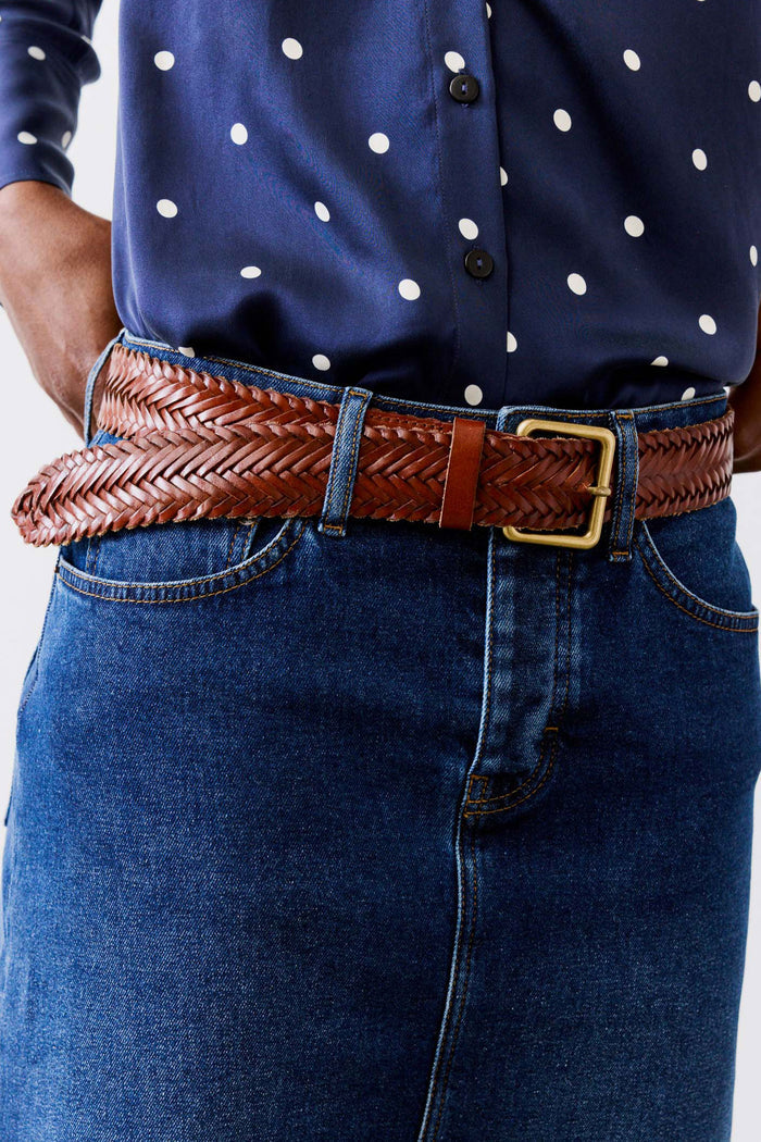Woven brown leather belt with brass buckle over blue jeans and dark shirt
