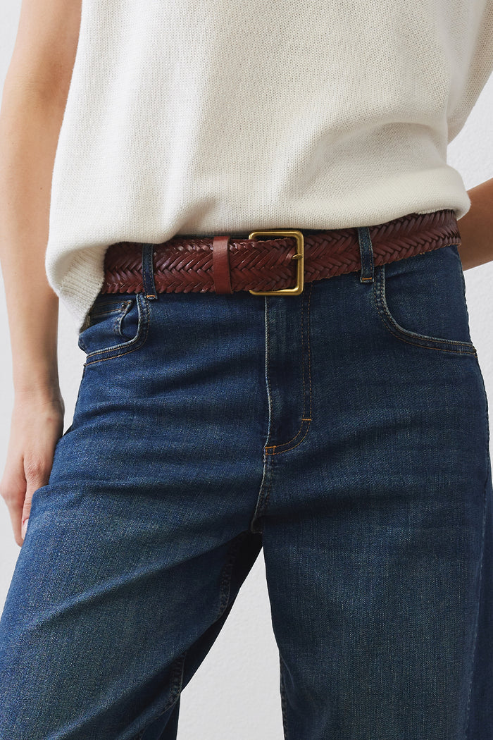 Brown leather belt with rectangular brass buckle on blue jeans waist