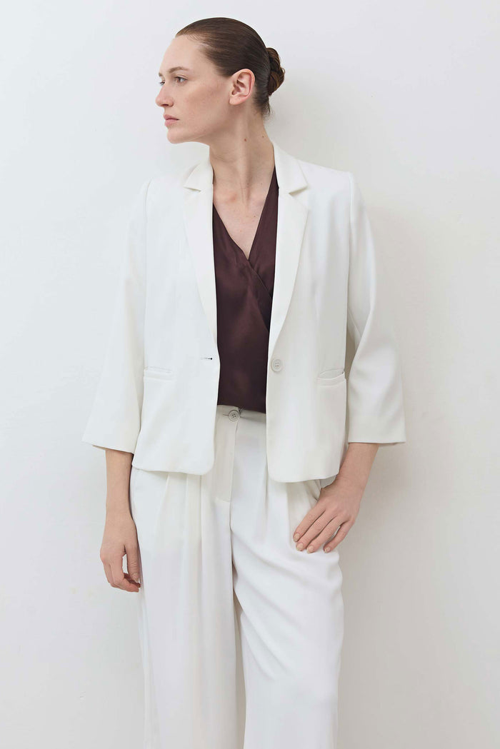White shrunken blazer with structured shoulders, notch lapel, and 3/4 sleeves.