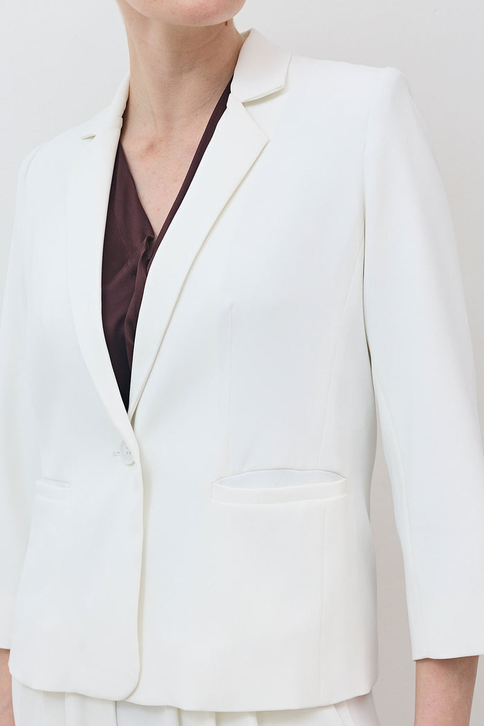 White shrunken blazer with notch lapel and welt chest pocket, 3/4 sleeves.