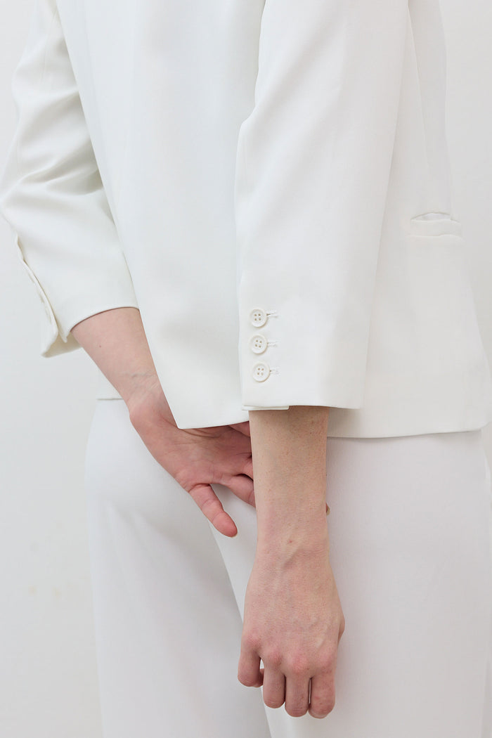 White shrunken blazer front with cropped hem and buttoned 3/4 sleeve cuff.