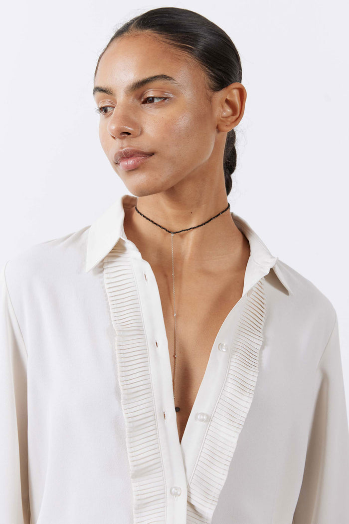 Close-up of off-white blouse neckline with pointed collar, buttons, and pleated trim