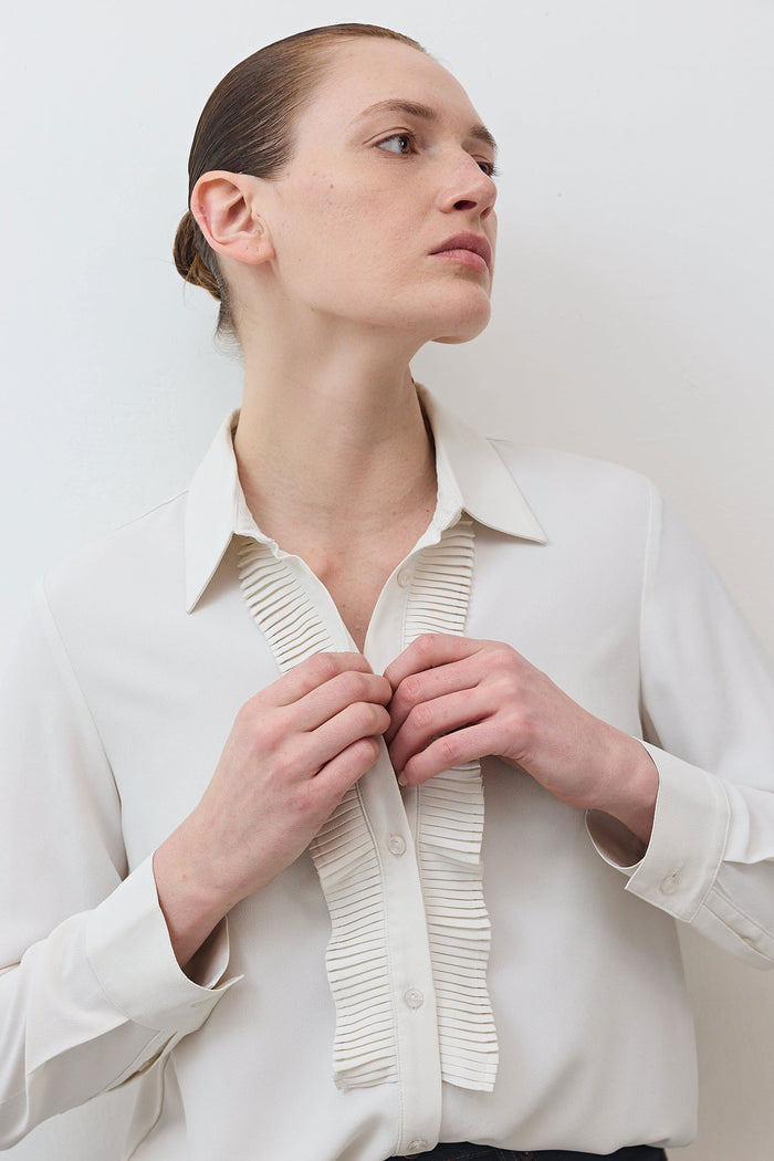 Close-up of off-white blouse collar with vertical pleated trim and button placket