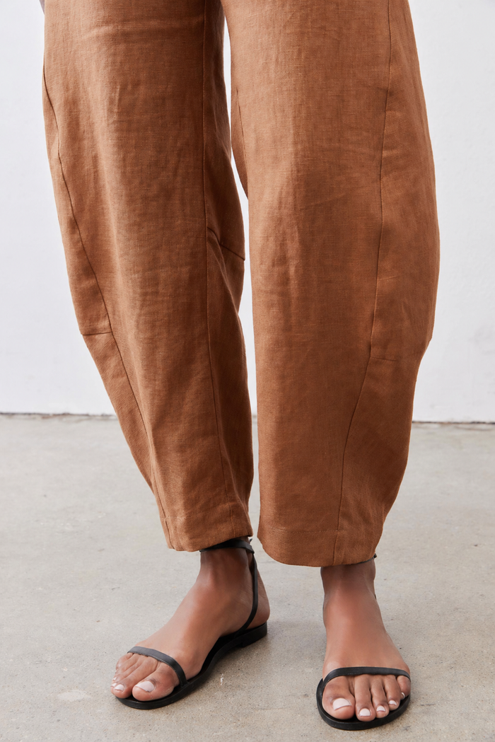 Caramel loose linen pants detail: wide legs, stitched seams, ankle-length hem.